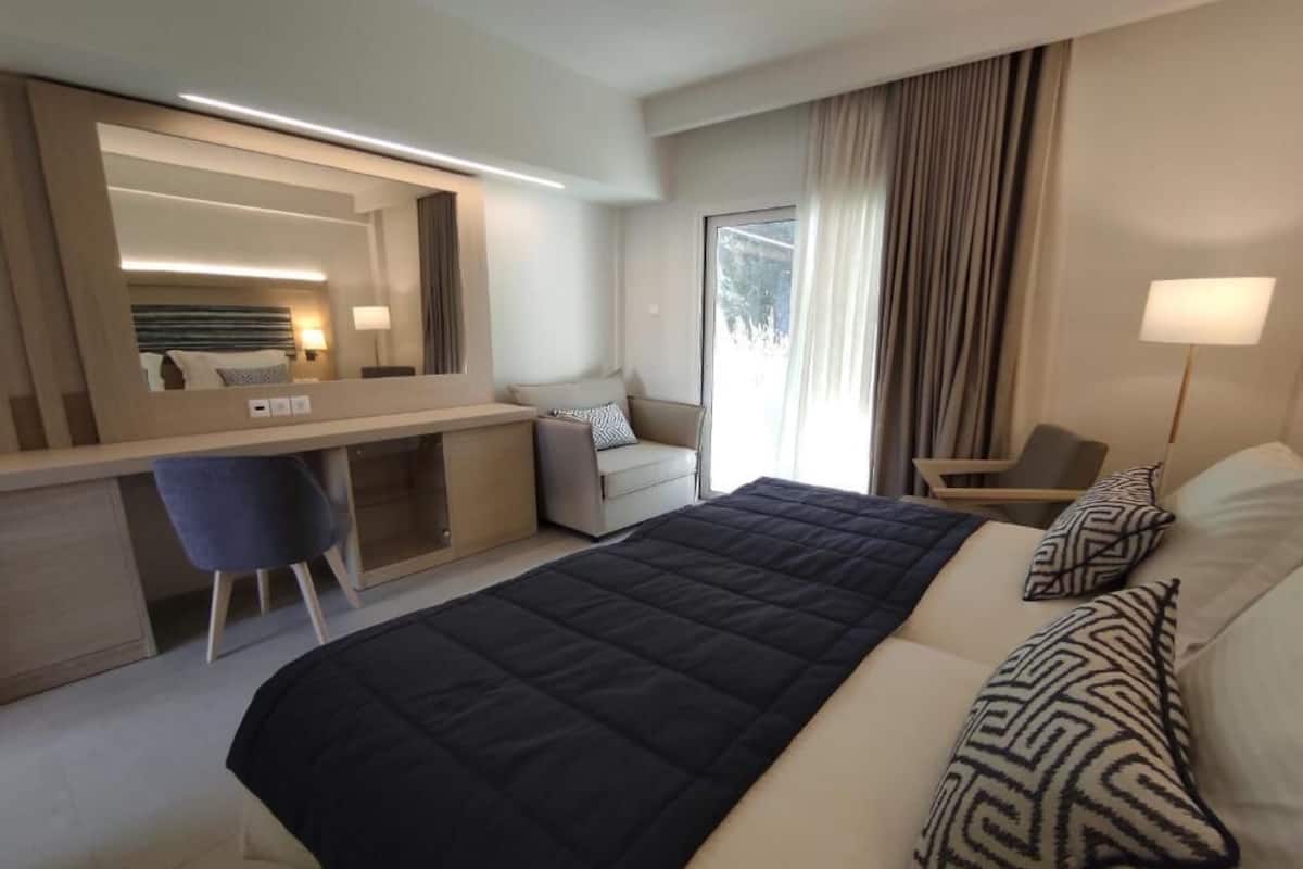 A modern hotel room with a large bed, a desk, a chair, and a large window with curtains.