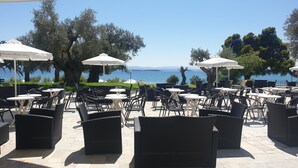 An outdoor seating area with tables and chairs, umbrellas, and a view of the sea. - O Paradise Beach Resort & Spa (Eretria)