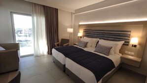 A modern hotel room with a large bed, two bedside tables with lamps, a chair, and a view of the outdoors through a large window. - O Paradise Beach Resort & Spa (Eretria)