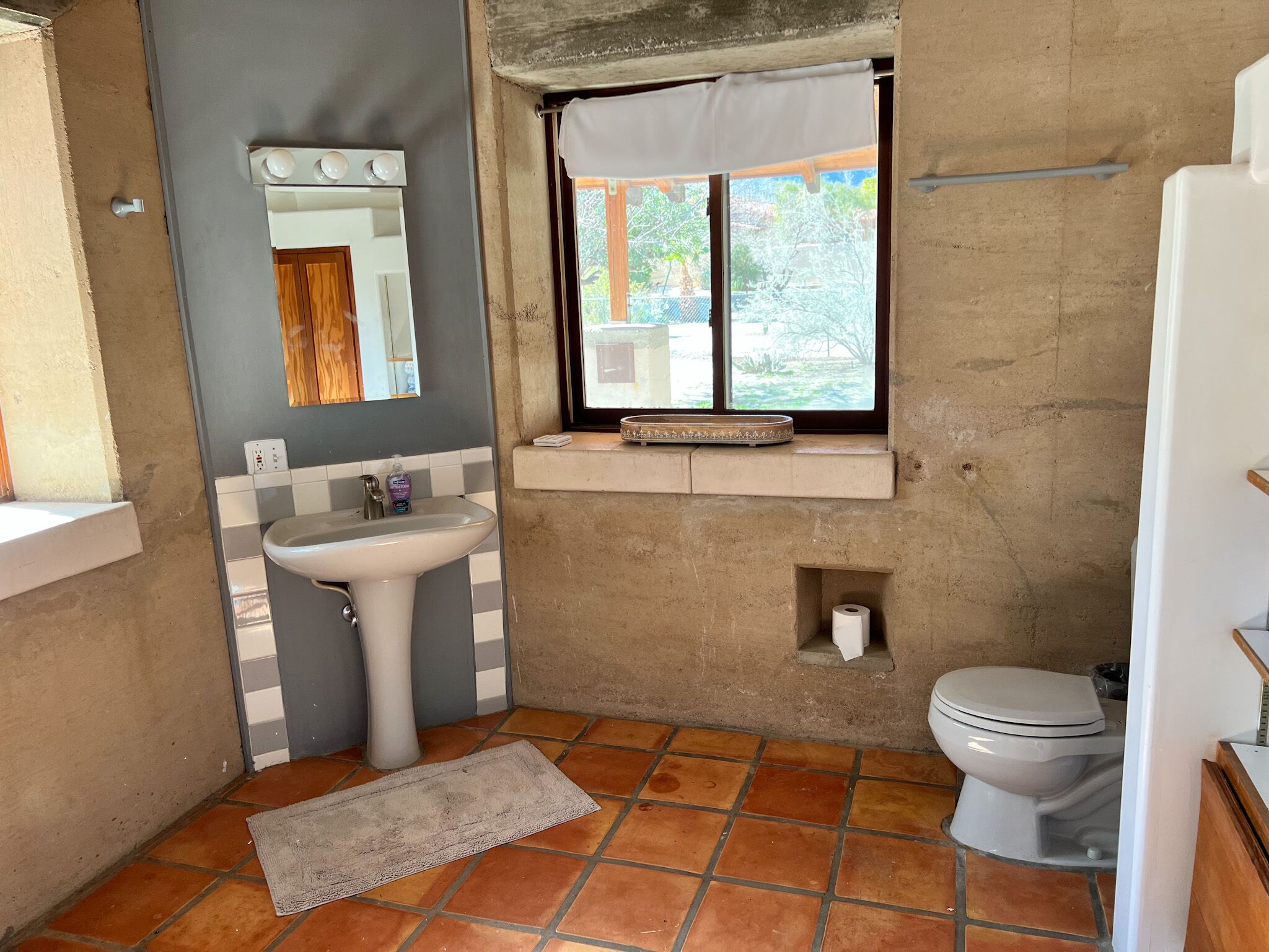 A compact bathroom with a pedestal sink, a toilet, and a small window with a curtain.