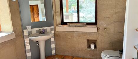 A compact bathroom with a pedestal sink, a toilet, and a small window with a curtain.