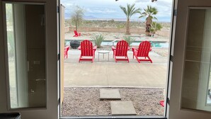 A view from inside a room to an outdoor patio with red Adirondack chairs, a small table, and a pool. - Majestic House with Unique Architecture, Forever Views, Pool, Spa, and Game Room (Borrego Springs)