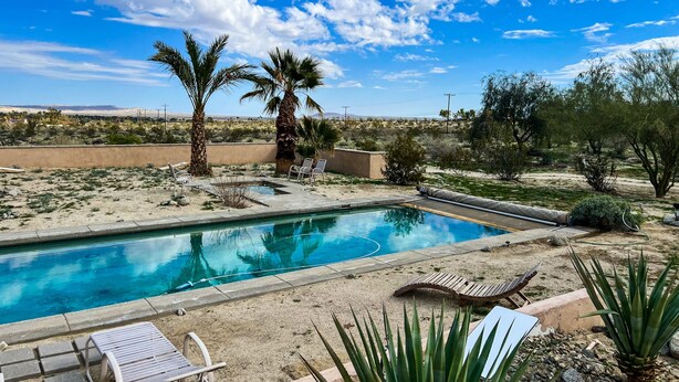 A pool area with lounge chairs, palm trees, and a desert landscape in the background. - Majestic House with Unique Architecture, Forever Views, Pool, Spa, and Game Room (Borrego Springs)