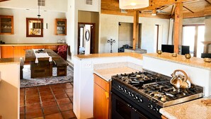 A kitchen with a gas stove, a refrigerator, wooden cabinets, and a dining area with a table and chairs. - Majestic House with Unique Architecture, Forever Views, Pool, Spa, and Game Room (Borrego Springs)