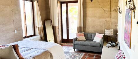 A bedroom with a bed, a sofa, a mirror, and a door leading outside.