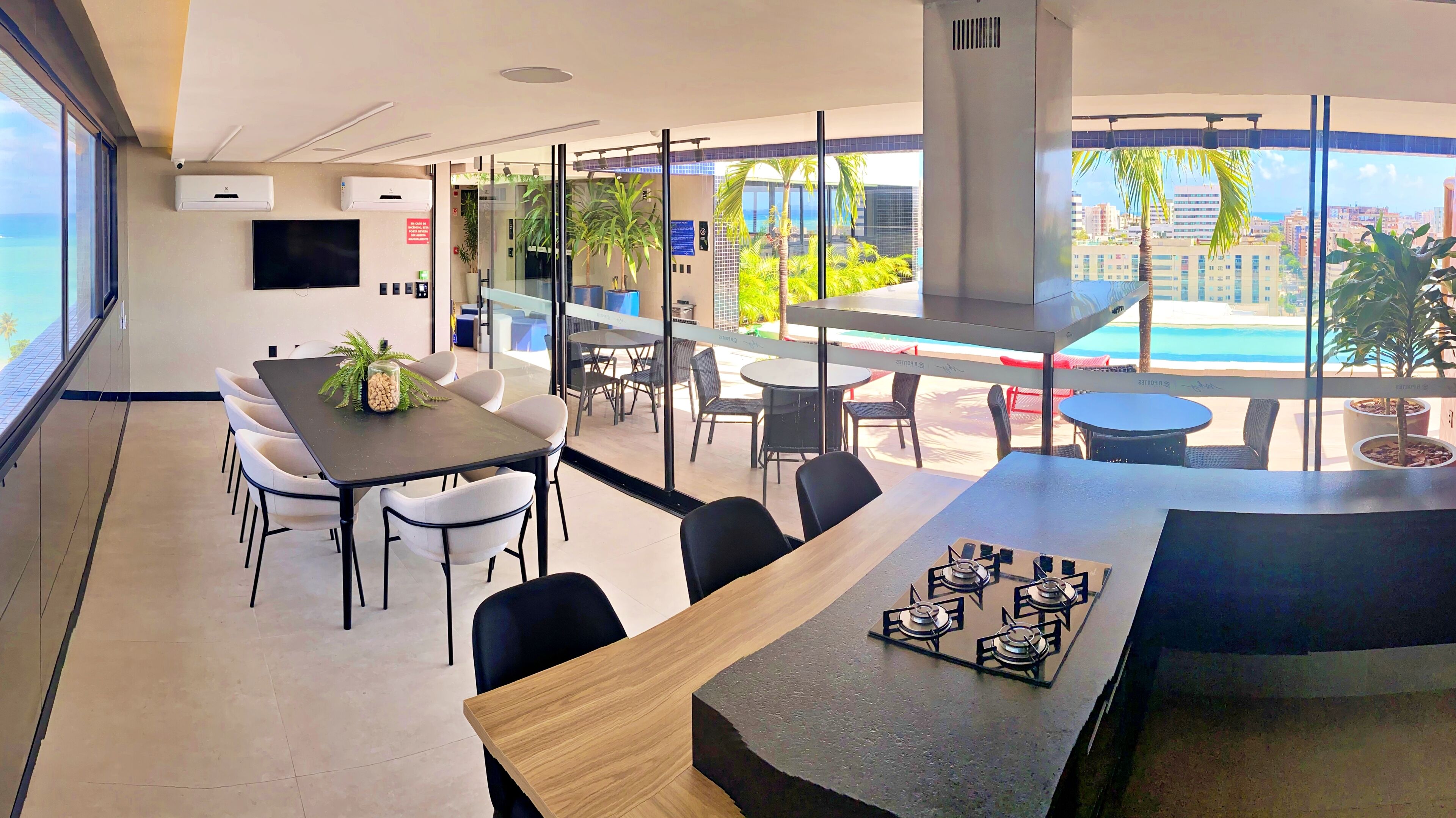 A modern hotel dining area with a large table, chairs, and a view of the city and ocean.