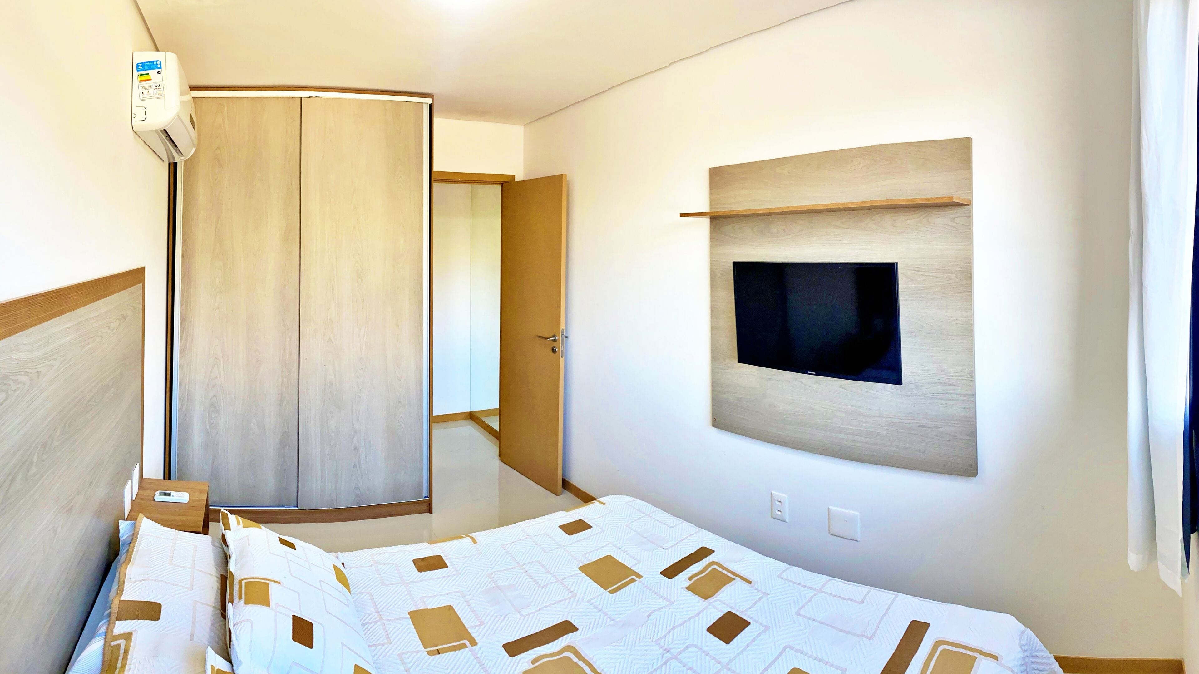 Un dormitorio moderno con una cama, un televisor montado en la pared y un armario.