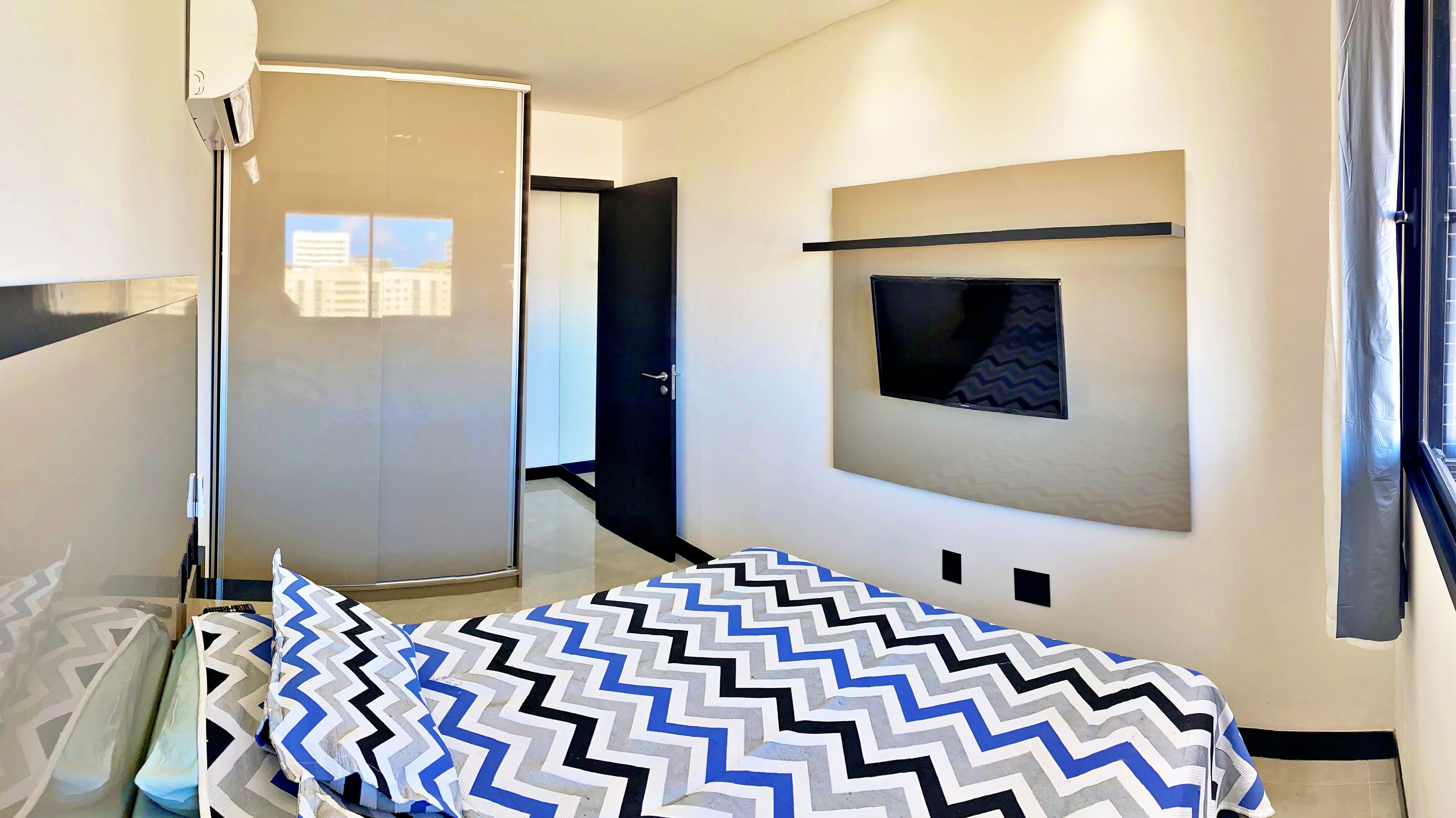 A modern bedroom with a bed, a TV mounted on the wall, and a sliding door leading to another room.