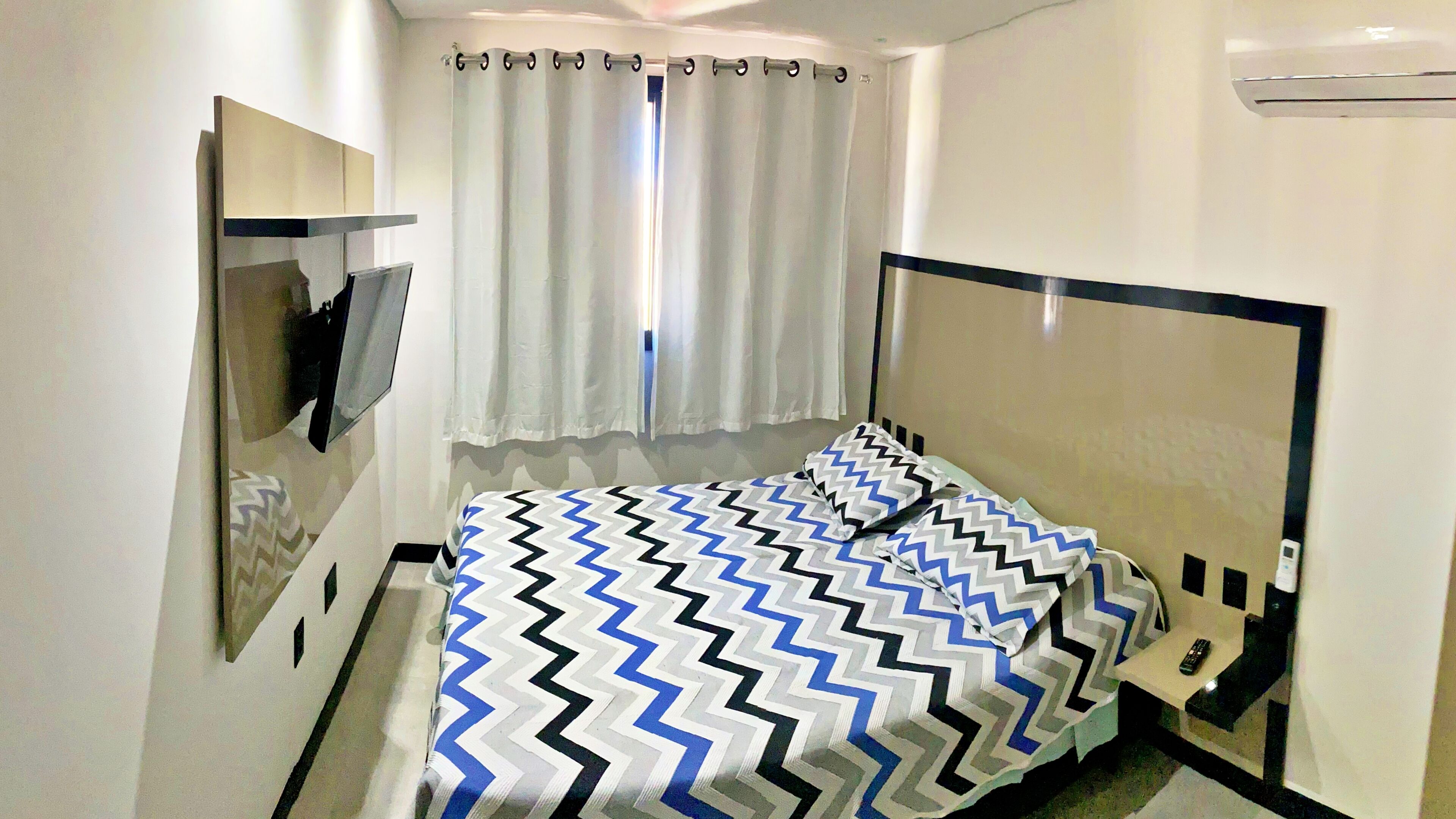 Ein Hotelzimmer mit Bett, Fernseher, Spiegel und einem Fenster mit Vorhängen.