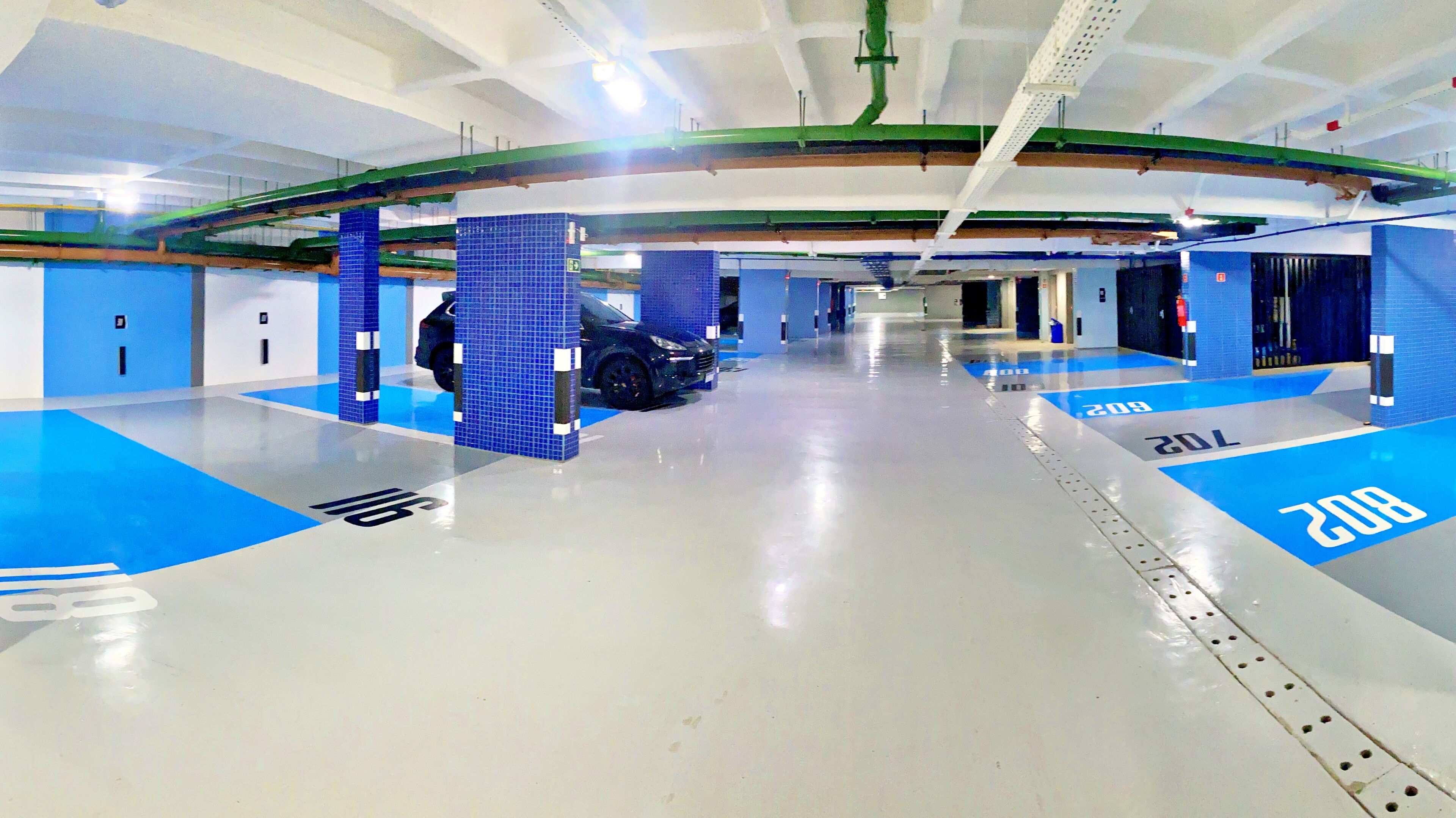 A parking garage with blue and white floor markings, a black car parked in a bay, and structural elements like beams and columns.