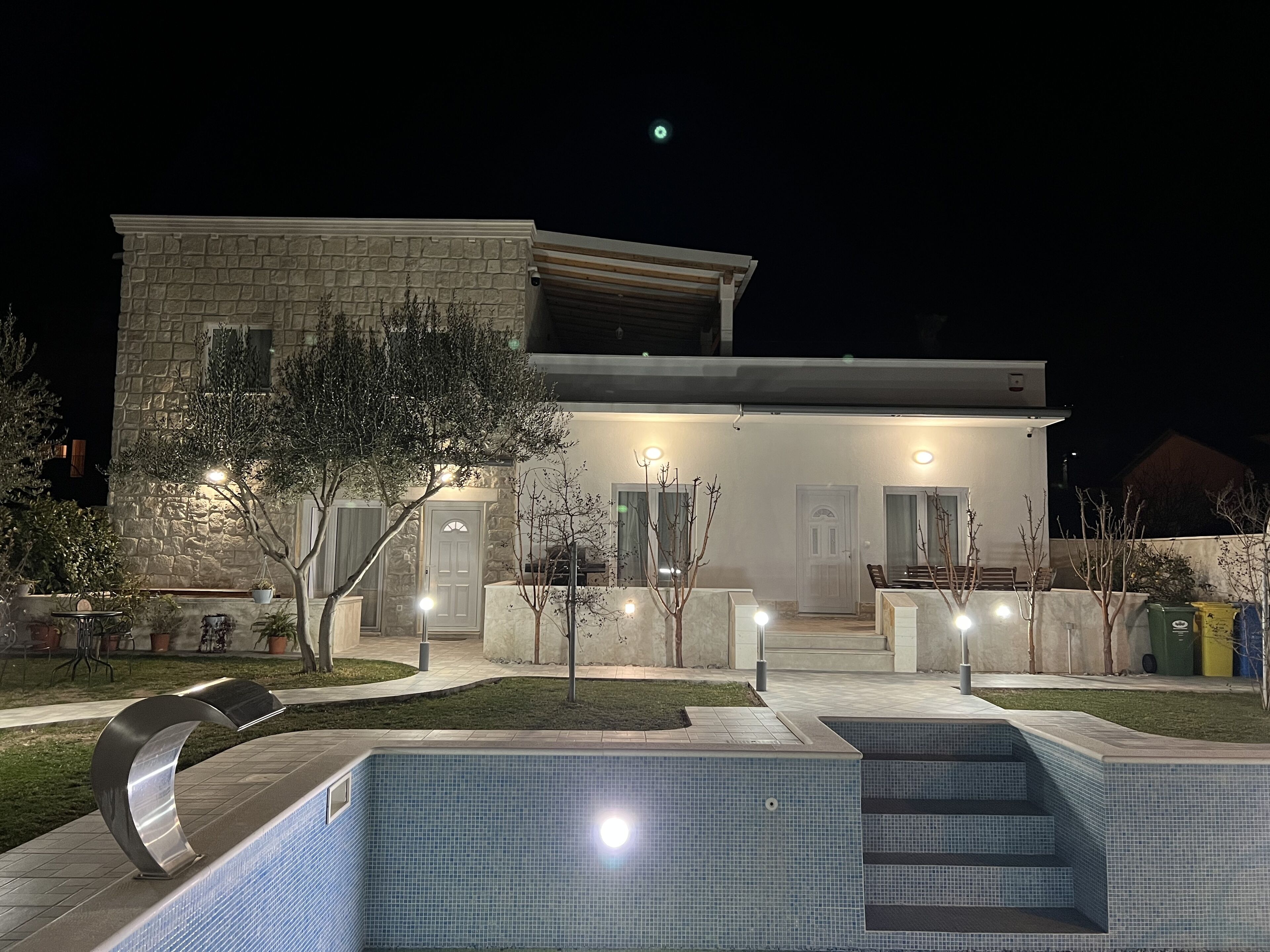 Une maison moderne dotée d’une piscine, d’une façade en pierre et d’un éclairage extérieur.