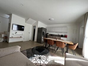 A modern living room with a sofa, a glass coffee table, and a TV mounted on the wall.