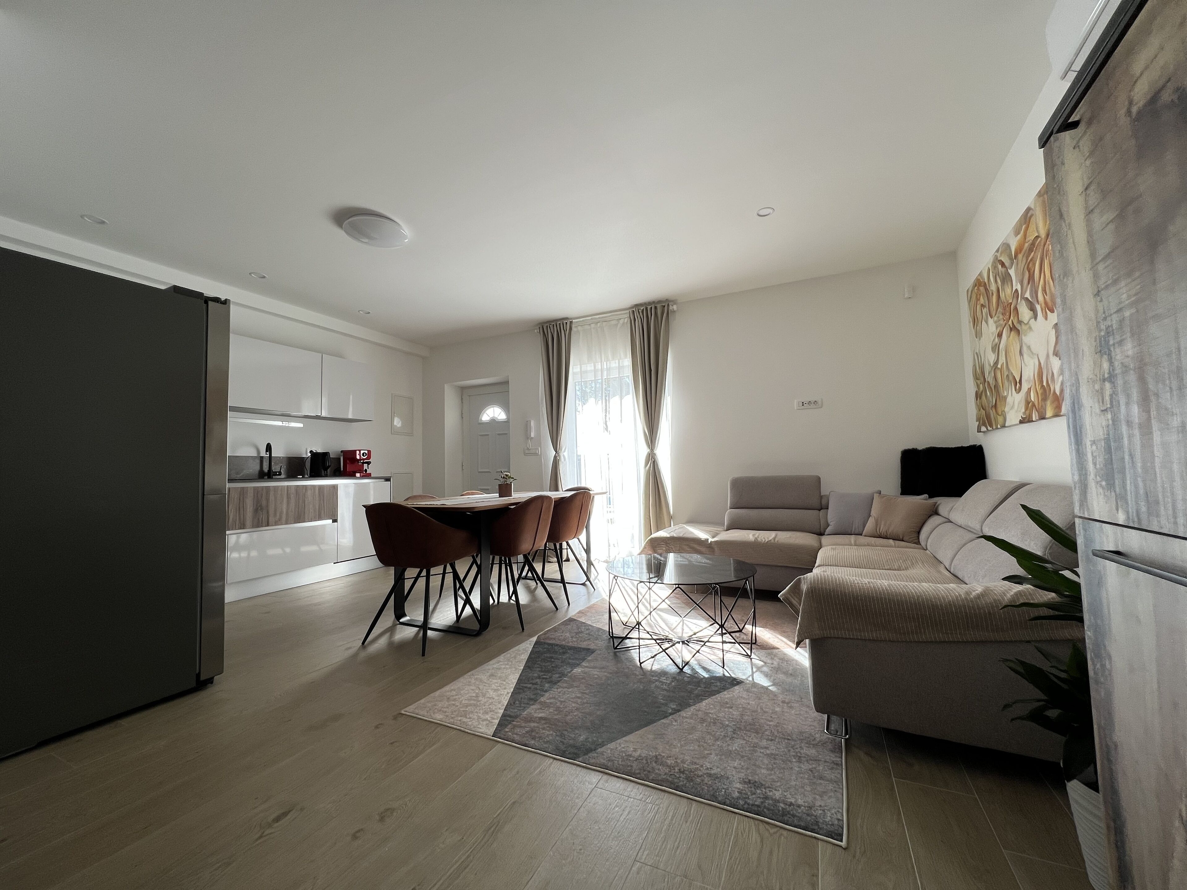 Una sala de estar moderna con un sofá, una mesa de comedor con sillas, una zona de cocina y un ventanal con cortinas.
