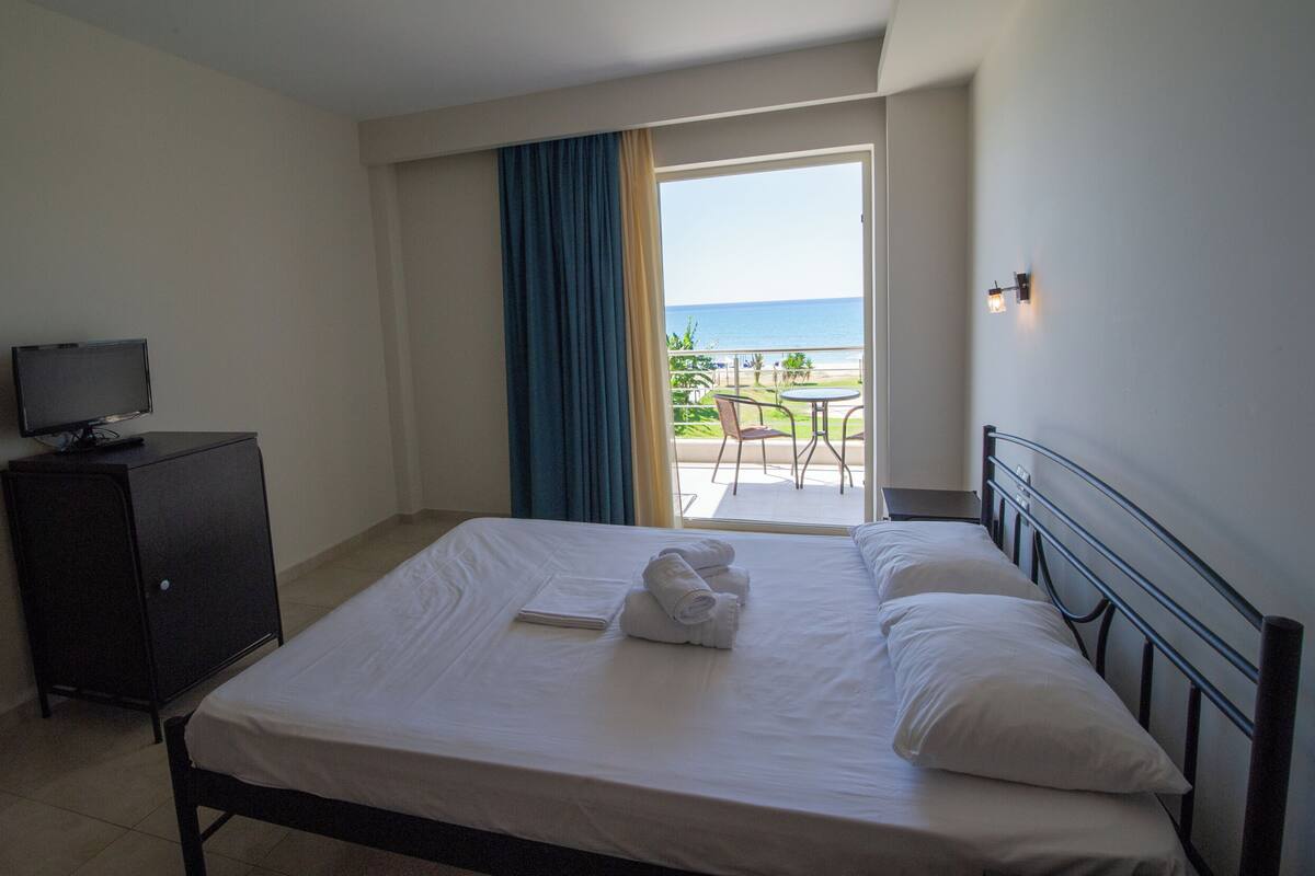 A hotel room with a bed, a television on a cabinet, and a view of the ocean through an open door.