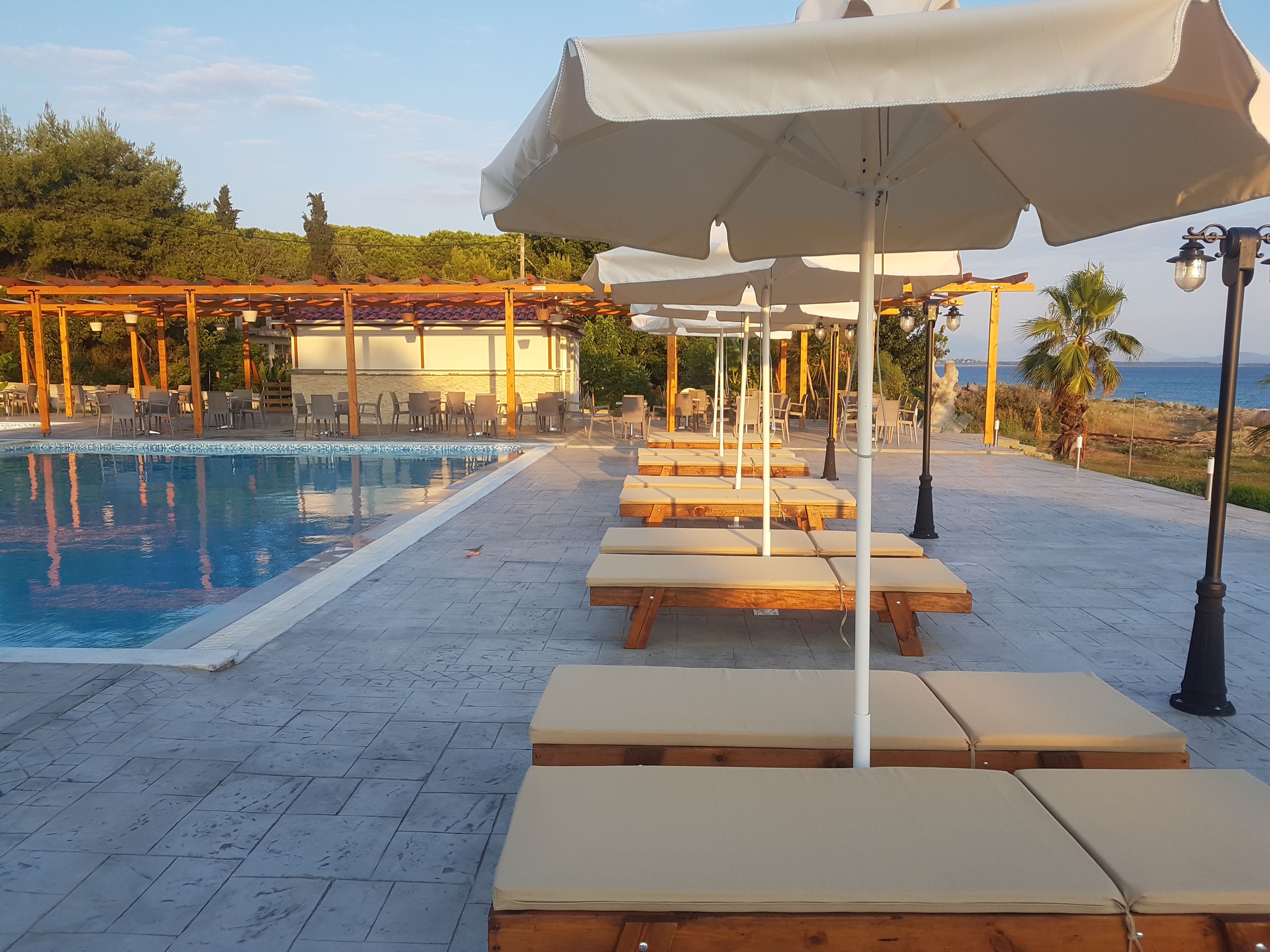 A poolside area with lounge chairs and umbrellas, a tiled deck, and a building in the background.