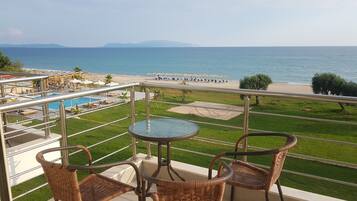 A balcony with wicker chairs and a table overlooking a pool and beach.