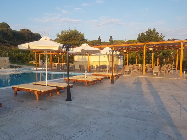 Un área junto a la piscina con sillones de descanso y sombrillas, una pérgola y una piscina.