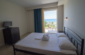 A hotel room with a bed, a television on a cabinet, and a view of the ocean through an open door. - Ocean Hotel (Preveza)
