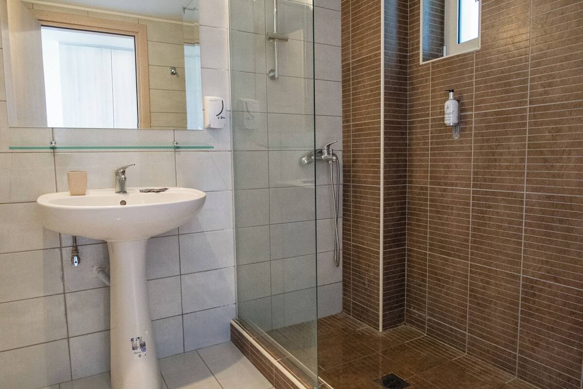 A bathroom with a glass-enclosed shower, a pedestal sink, and a mirror above the sink.
