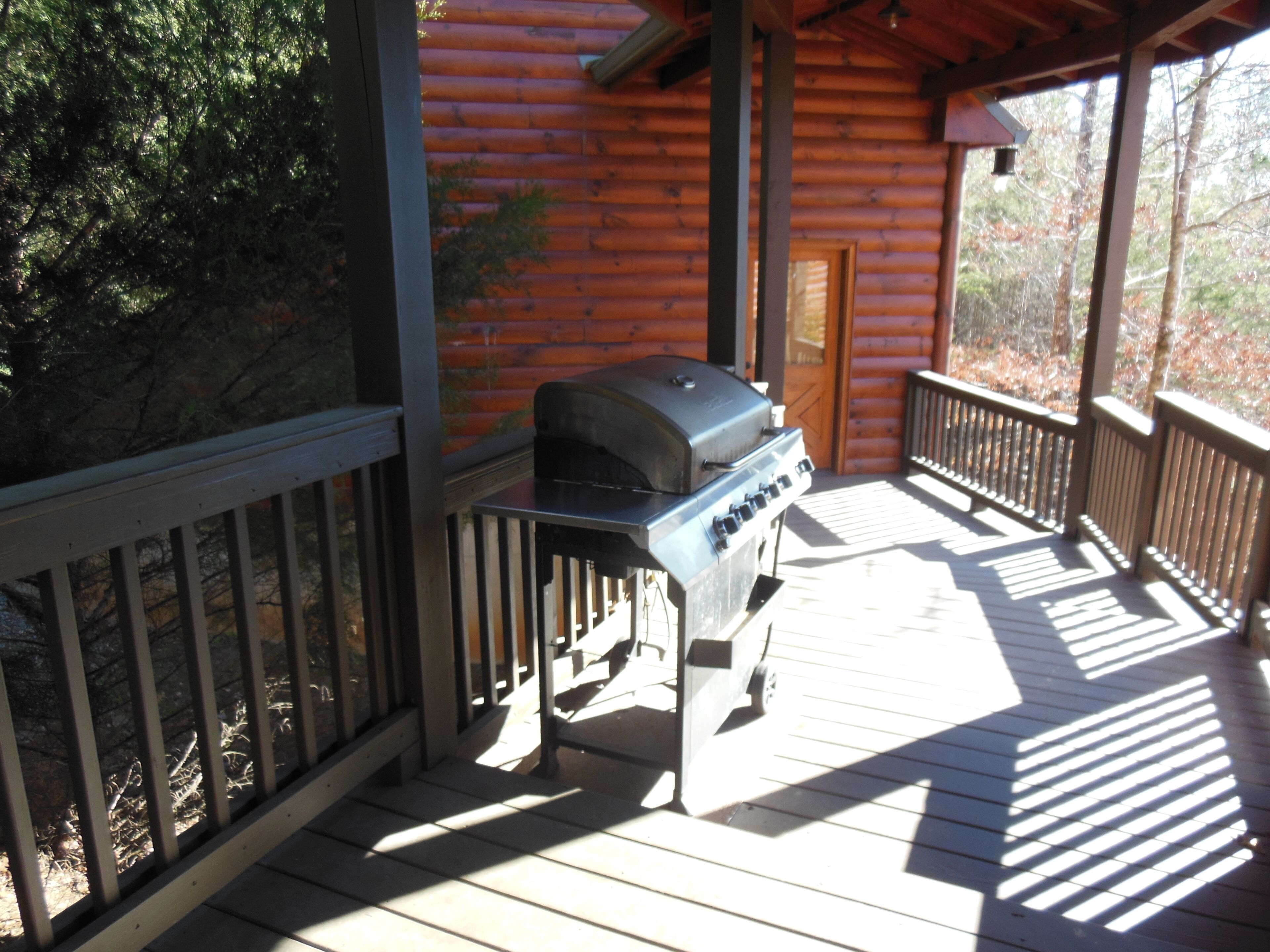 An outdoor grill on a wooden deck with a view of a log cabin.