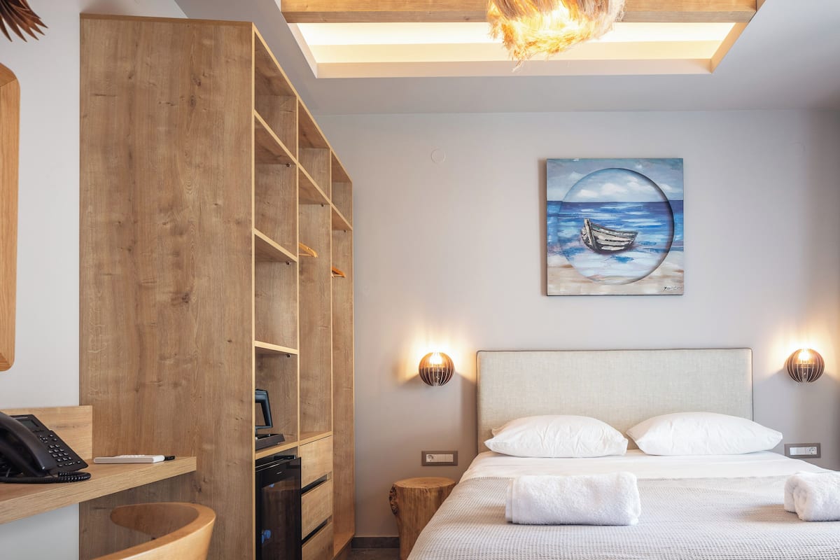 Un dormitorio con cama, lámparas de noche, un cuadro de un barco en el agua y un armario de madera.