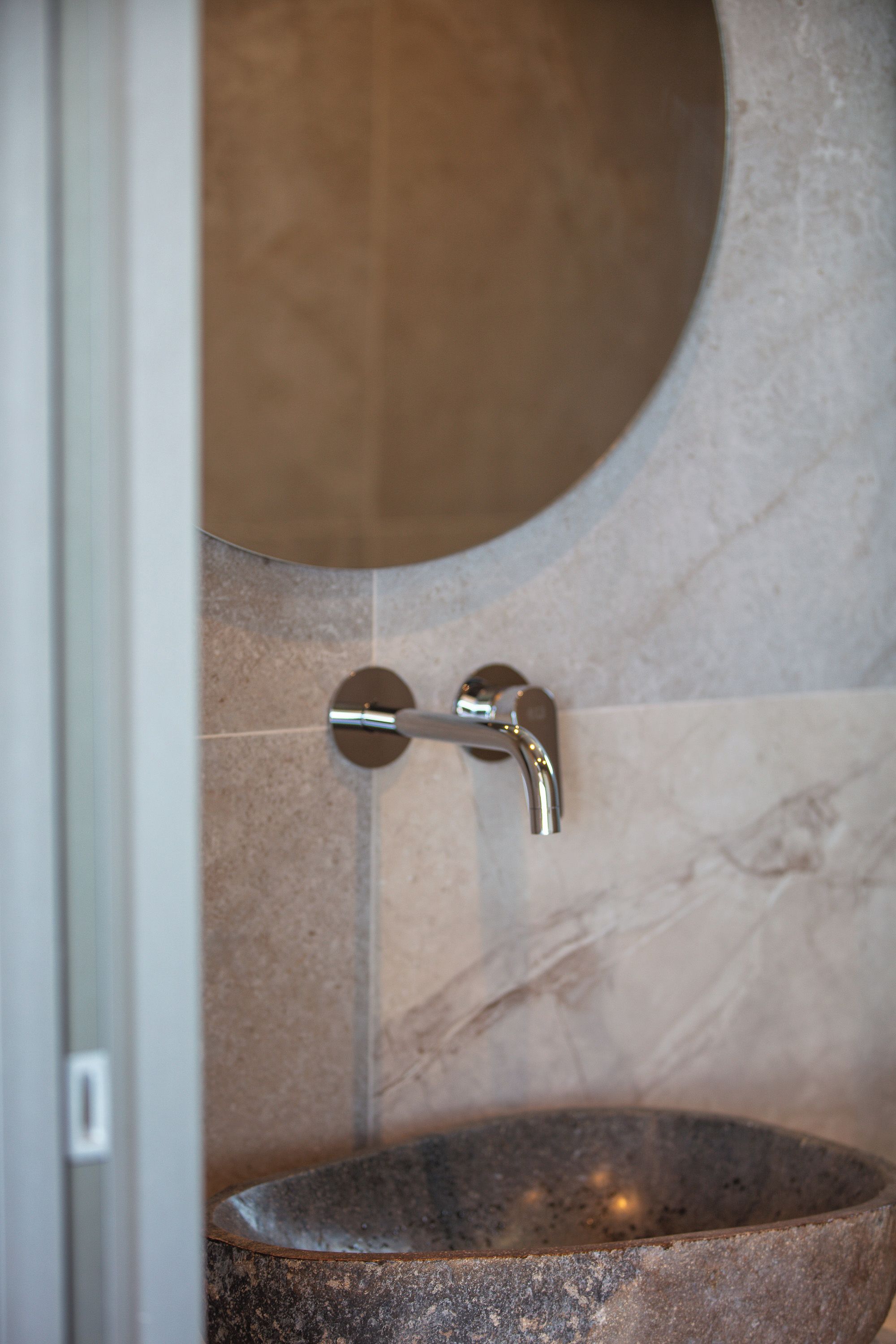 A bathroom with a stone sink, a round mirror, and a modern faucet.