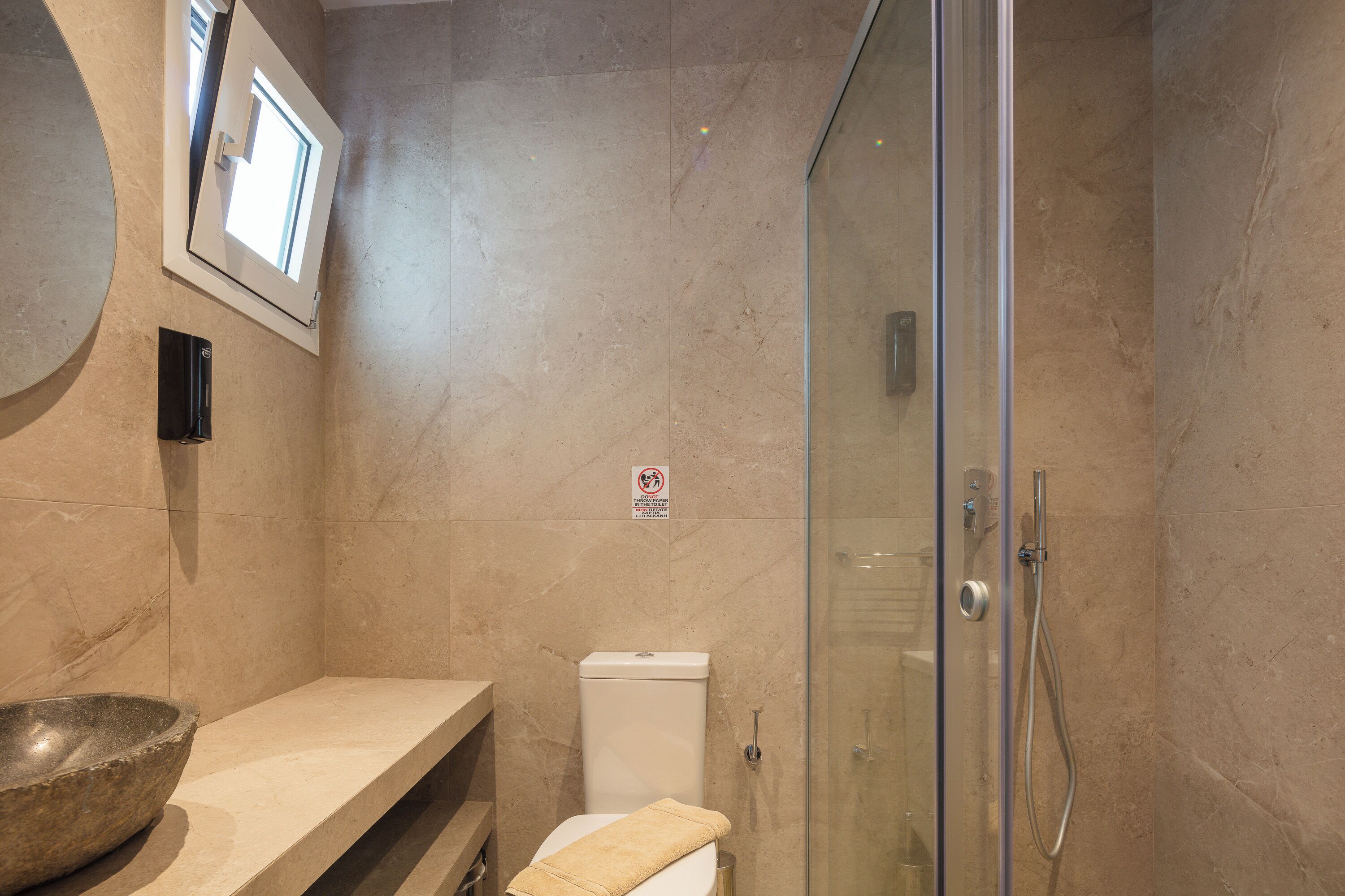 A bathroom with a glass shower enclosure, a toilet, a sink with a bowl, and a towel.