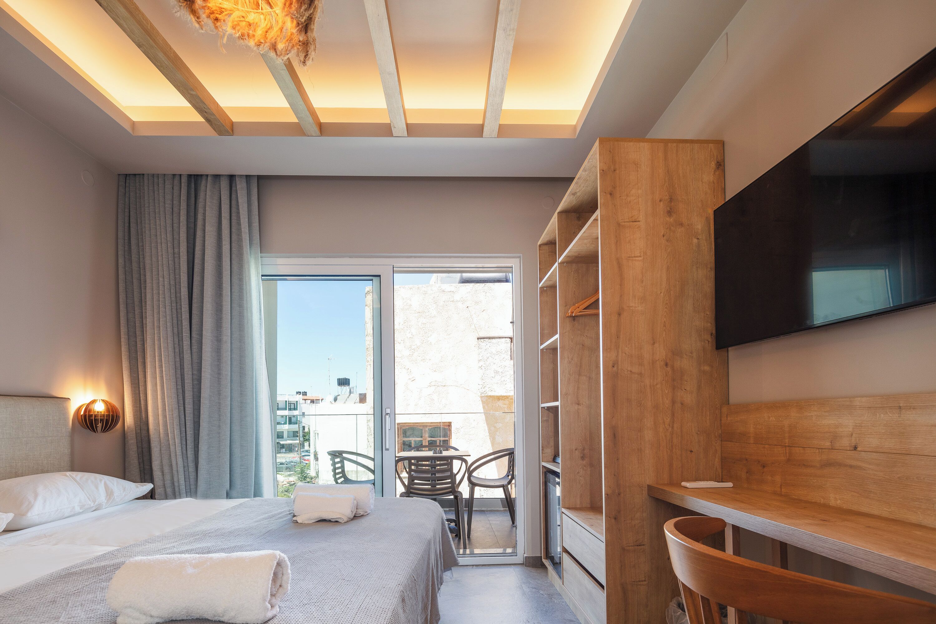 A hotel room with a bed, a desk, a TV, and a balcony with a table and chairs.