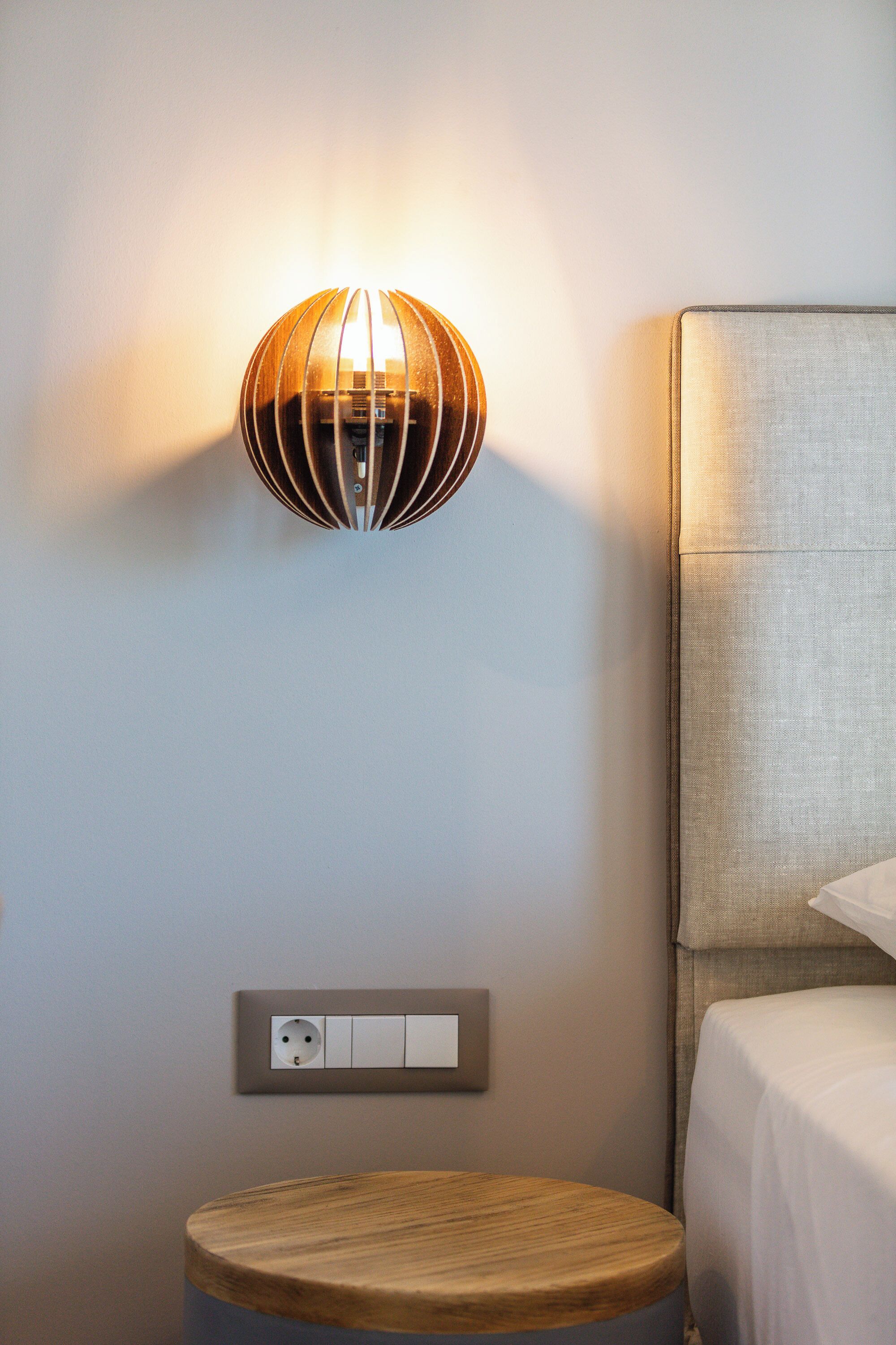 A modern room with a wall-mounted light fixture, a bedside table, and a bed with a headboard.