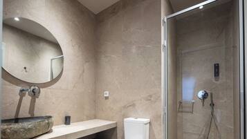 A bathroom with a large oval mirror, a stone sink, a toilet, and a glass-enclosed shower area.