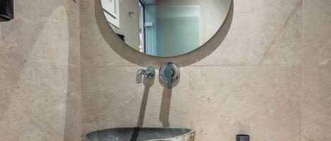 A bathroom with a stone sink, a round mirror, and a small cup on the counter.