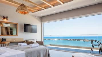A modern bedroom with a large window, a flat-screen TV, and a view of the sea.