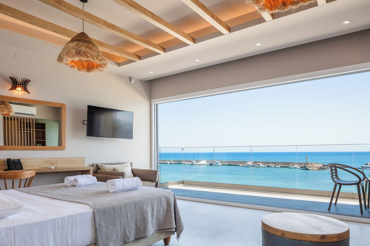 Una habitación de hotel moderna con un balcón amplio, una cama, un escritorio y un televisor.