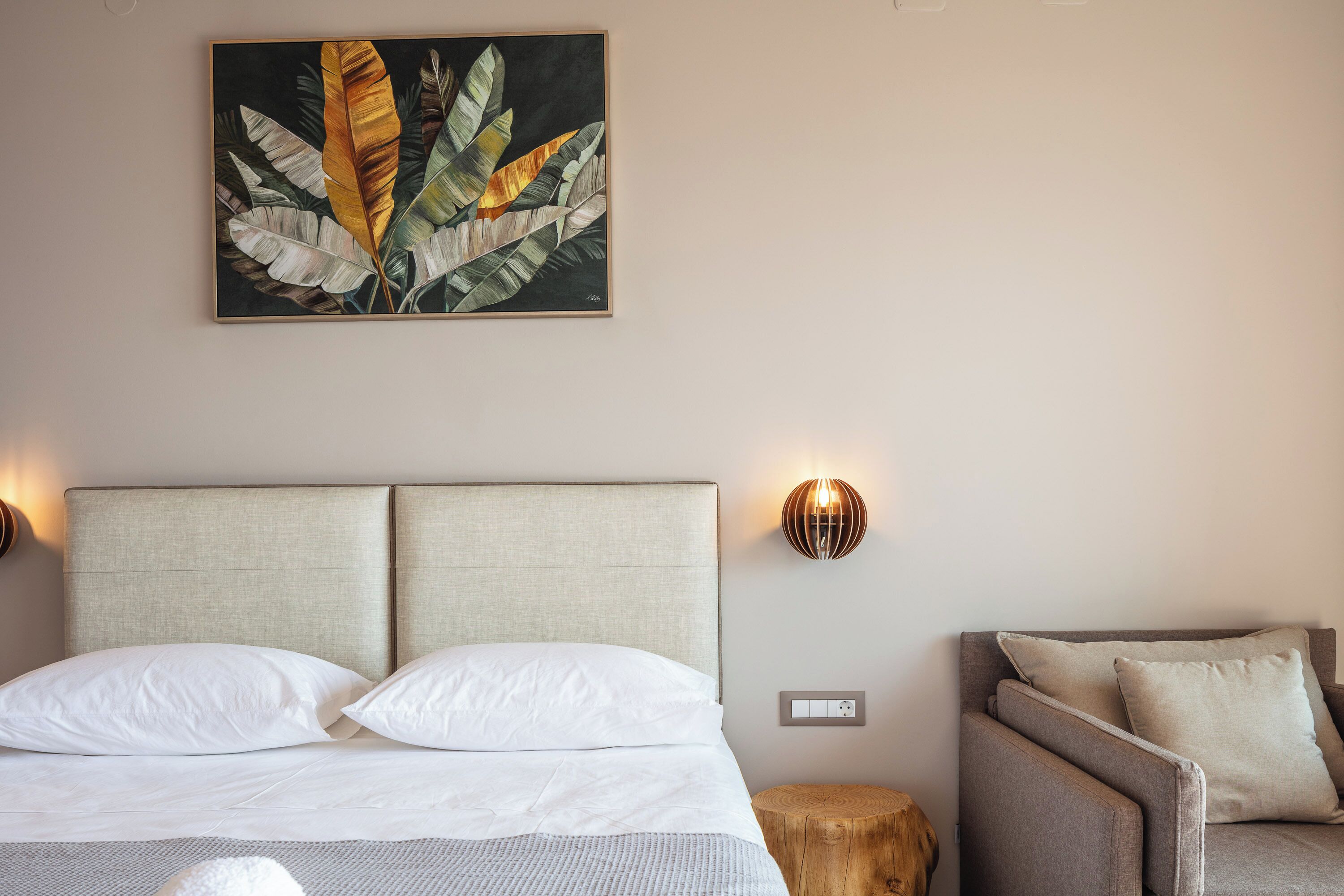 Een hotelkamer met een bed, nachtkastje, een houten kruk, een bank en een wandlamp.