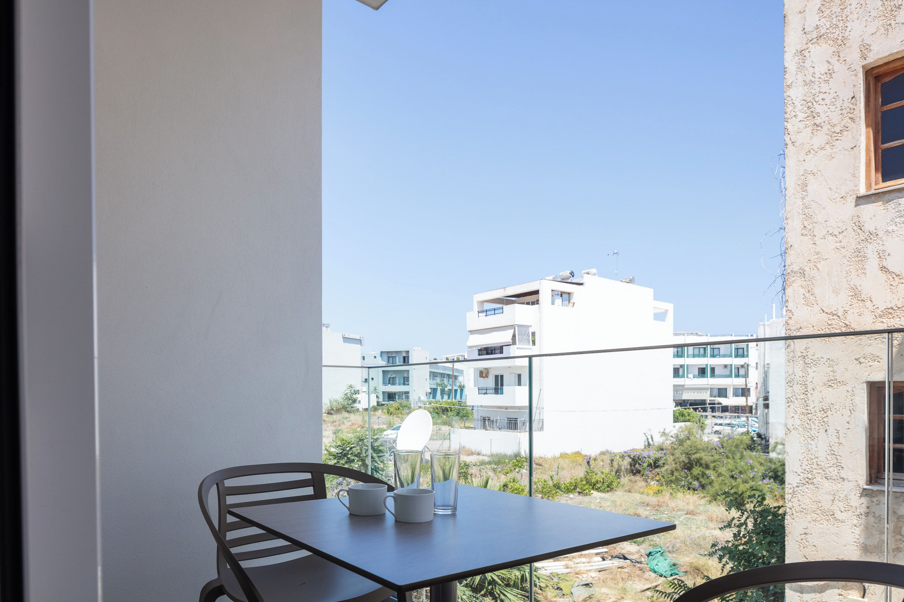 Un balcone con tavolo e sedie, vista su un panorama urbano con edifici moderni.