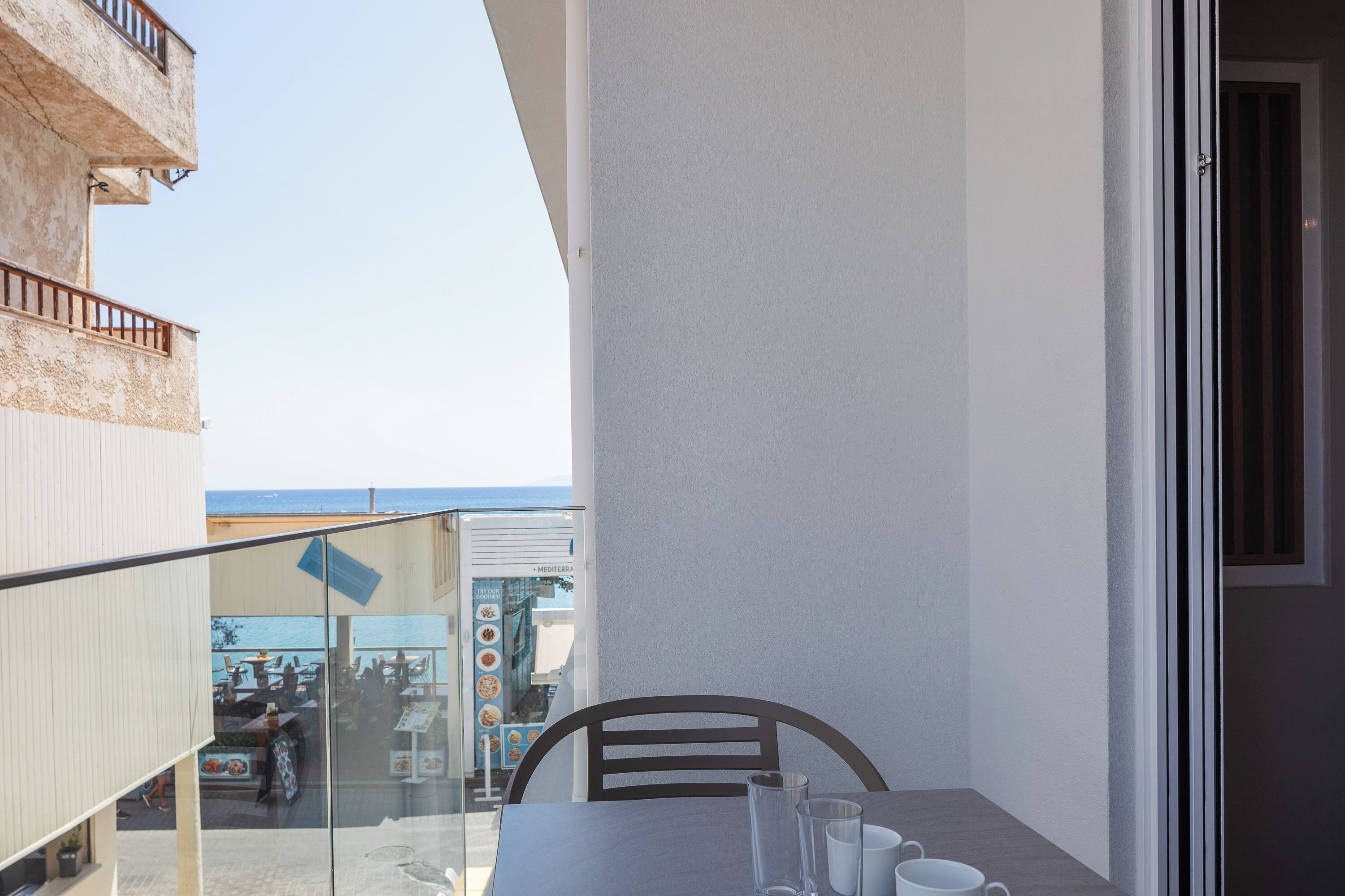 A balcony with a table and chairs, overlooking a dining area with a view of the sea.