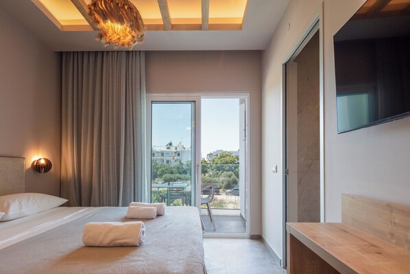 Quarto de hotel moderno com uma cama grande, um banco de madeira, uma TV e uma varanda com vista para a cidade.