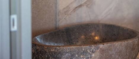 A bathroom with a stone sink, a curved mirror, and a chrome faucet.
