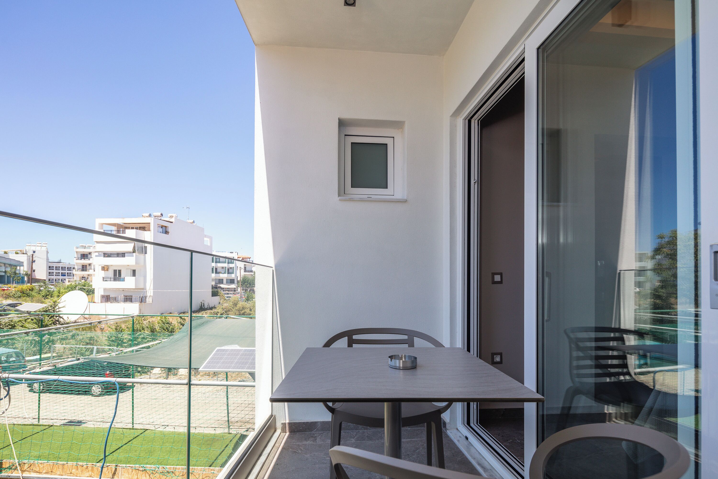 Ein Balkon mit Tisch und Stühlen, ein kleines Fenster und Blick auf die umliegenden Gebäude.