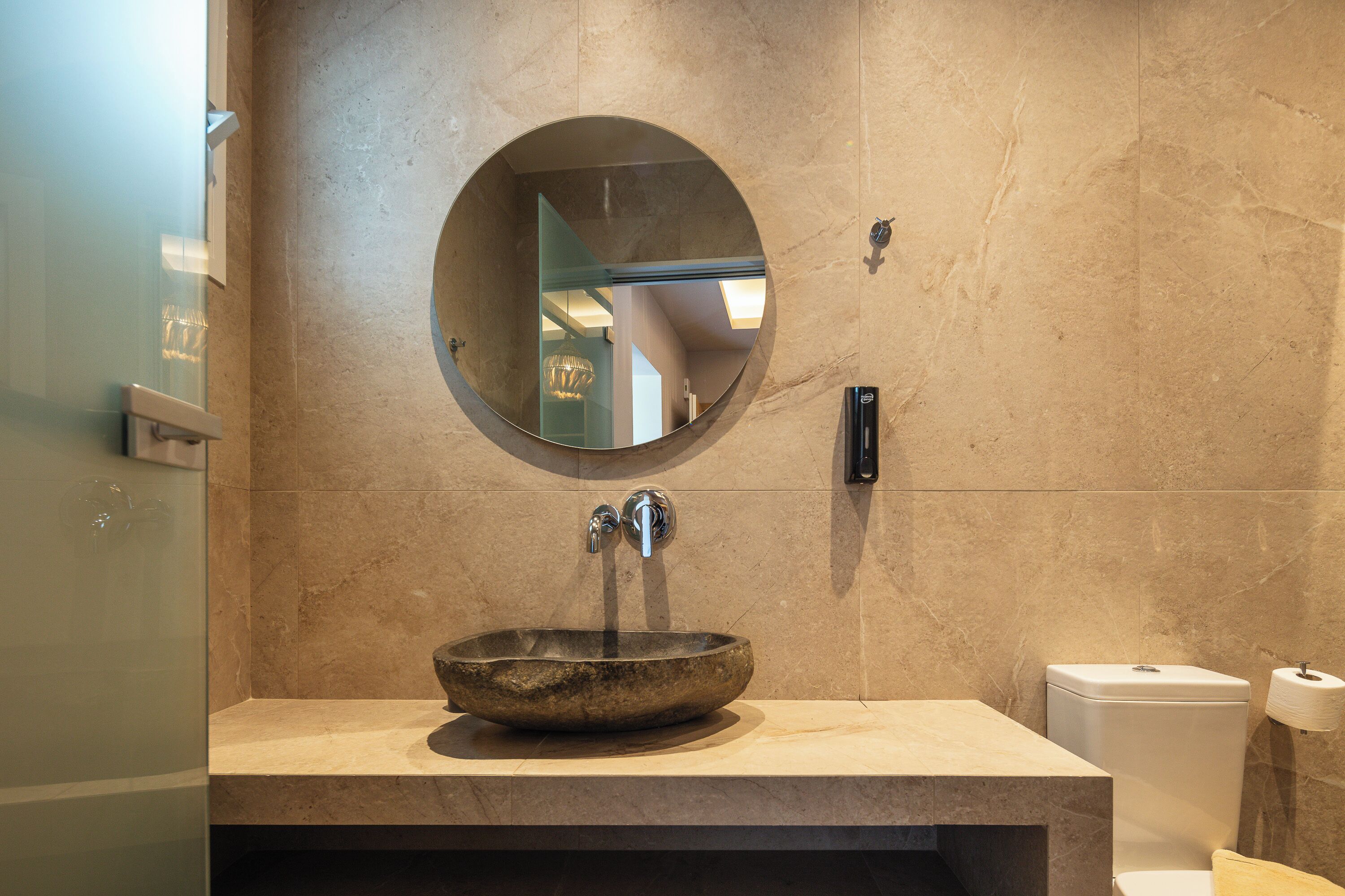 Une salle de bain avec un miroir rond, un lavabo en pierre et des toilettes.