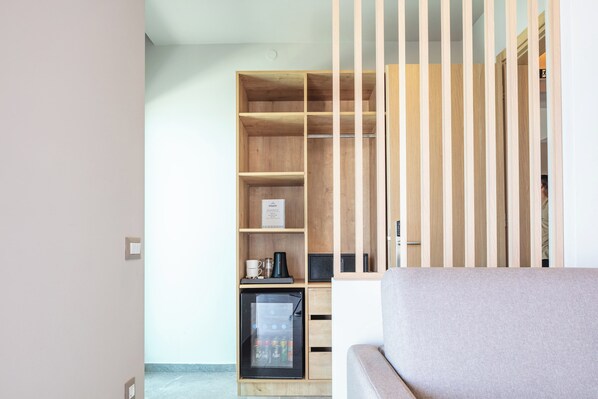 A modern living room with a built-in wooden shelving unit, a compact refrigerator, and a sofa. - Skipper Beachfront Suites (Hersonissos)