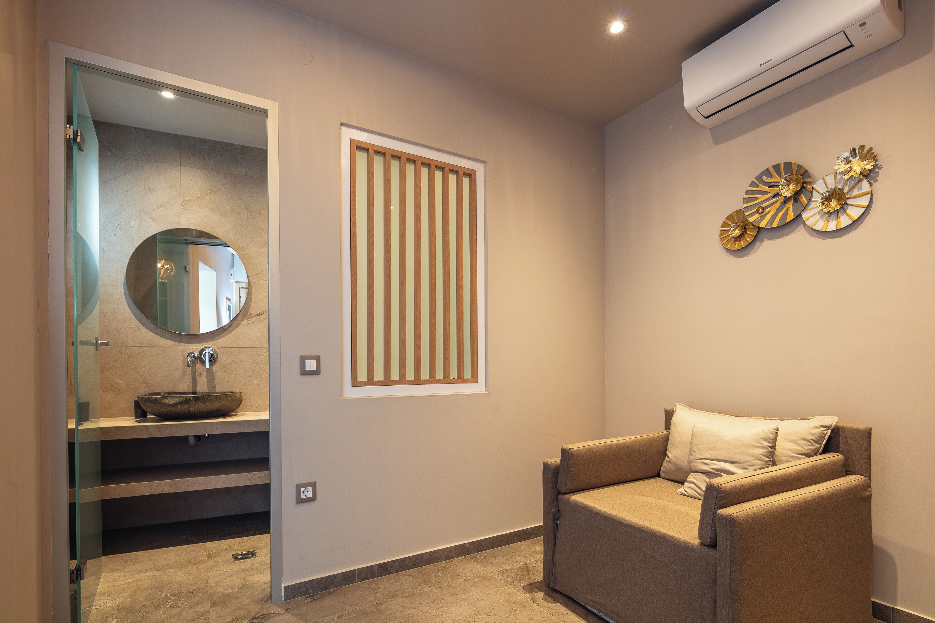 A modern bathroom with a glass-enclosed shower, a round mirror, a vessel sink, and a wall-mounted air conditioner.