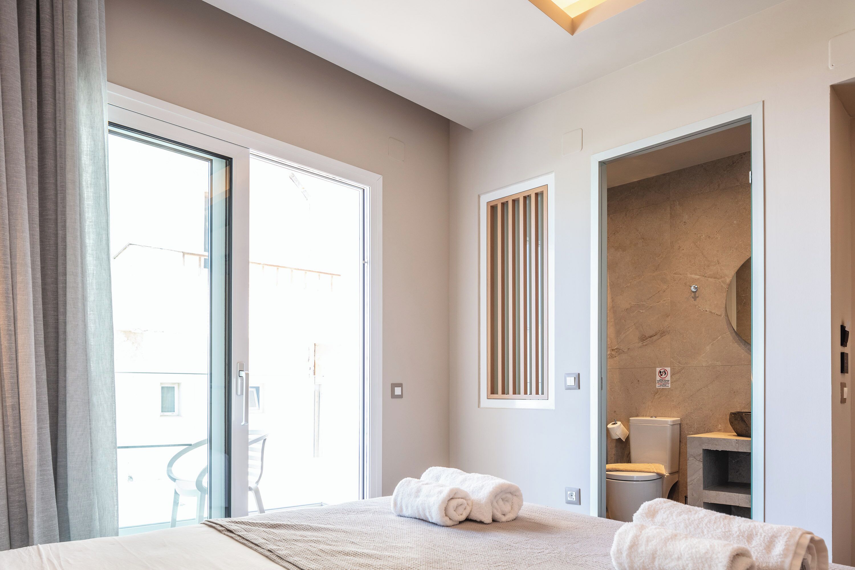 Ein Hotelzimmer mit Bett, einem Badezimmer mit Toilette und Waschbecken sowie einem Balkon mit einem Stuhl.