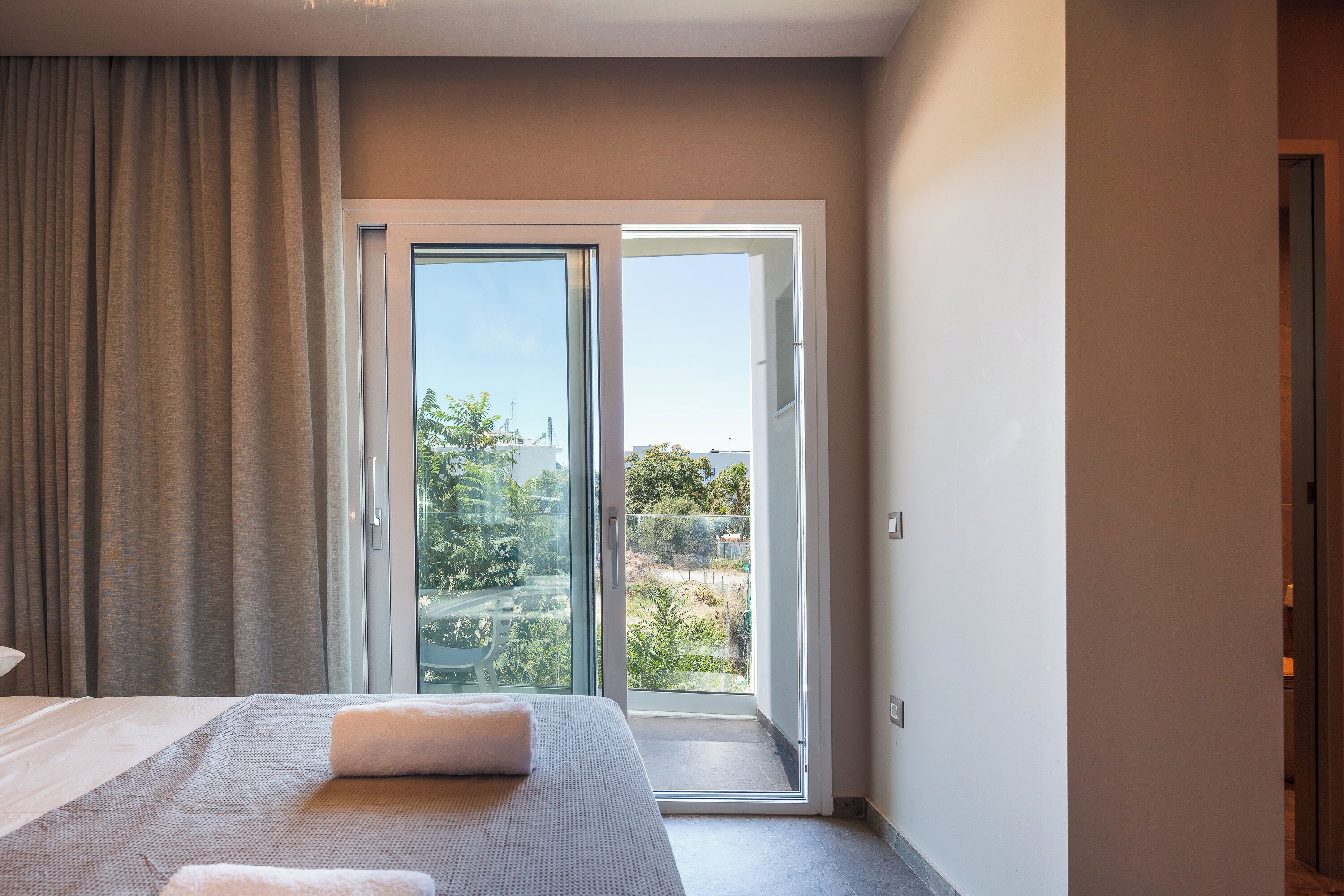 Un dormitorio con una cama grande, una puerta corrediza de vidrio que da a un balcón y vistas a zonas verdes.