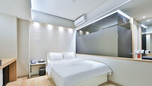 Una habitación de hotel moderna con una cama grande, una mesita de noche con teléfono y un cesto de basura, un espejo y un equipo de aire acondicionado en la pared.