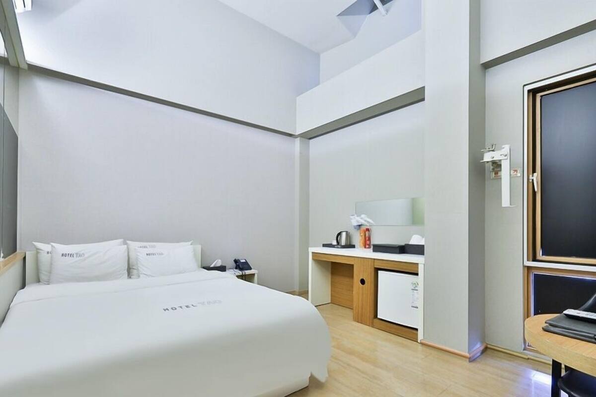Quarto de hotel moderno com uma cama grande, uma escrivaninha com computador e uma janela com vista para o céu.