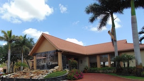 A hotel with a red-tiled roof, a stone waterfall feature, and a brick pathway leading to the entrance. - Vacation in Paradise, Naples, FL (Naples)