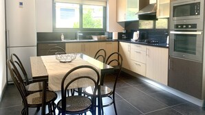 A modern kitchen with a dining table, chairs, a refrigerator, a window, and built-in appliances. - Villa Bella (Machico)