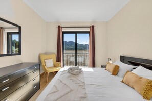 Une chambre d’hôtel avec un lit, une chaise, une commode et une grande fenêtre donnant sur les montagnes.