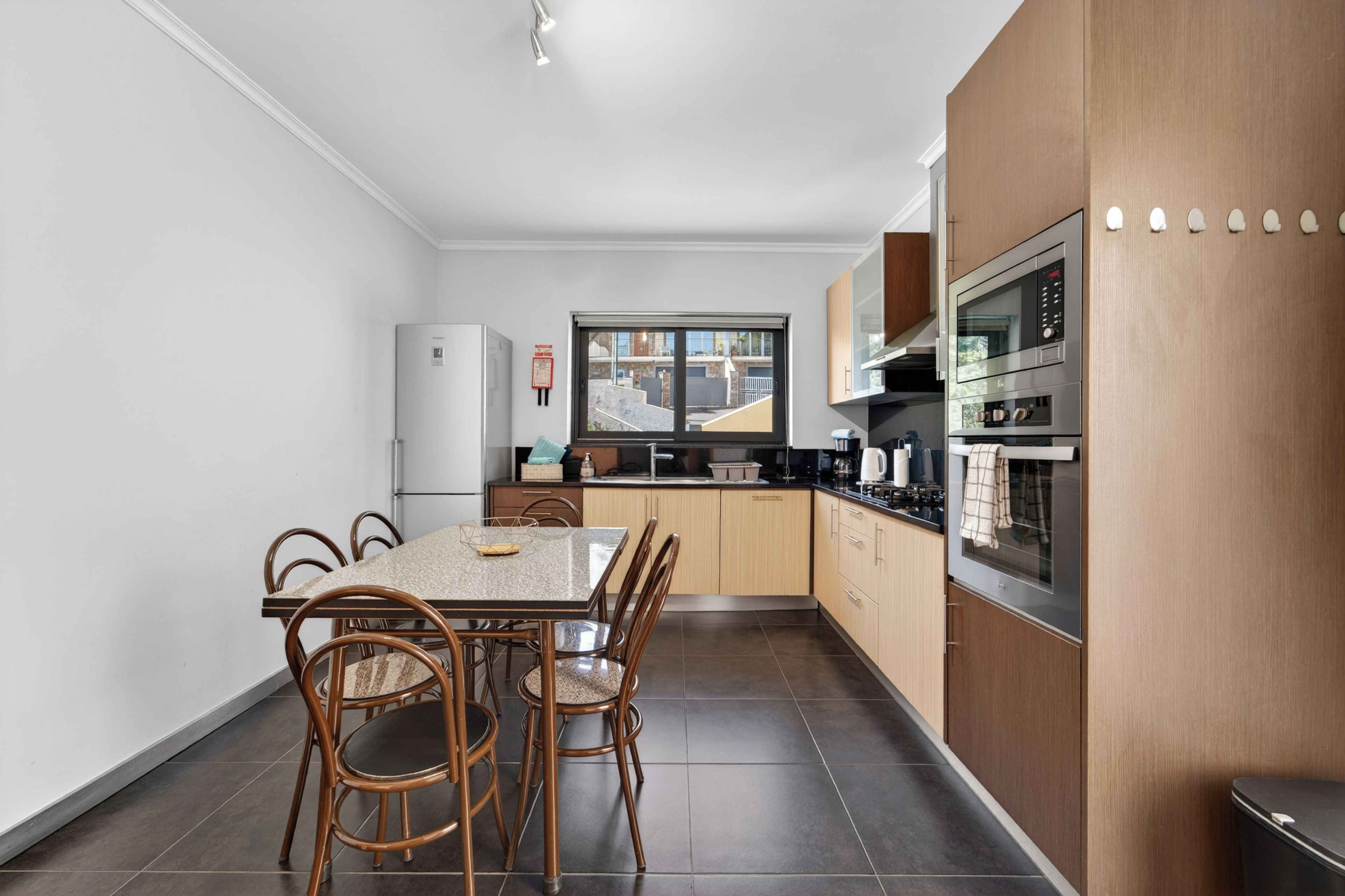 A modern kitchen with a dining area, featuring a large window, stainless steel appliances, and a clean, minimalist design.